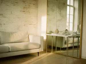 Compacte woonkamer met vloerspiegel die natuurlijk licht weerkaatst, linnen bank, marmeren sidetable en warme ivoor- en saliegroen tinten.
