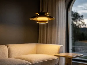 Sculptuurachtige hanglamp met warm gouden licht boven een crème bouclé bank, travertijn bijzettafel en linnen gordijnen in een stijlvolle woonkamer.