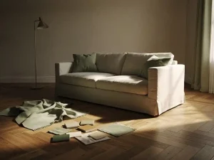 Onafgewerkte woonkamer met linnen bank op onhandige hoek, stoffenstalen en verfchips op visgraat eiken vloer, staande lamp met warm licht.
